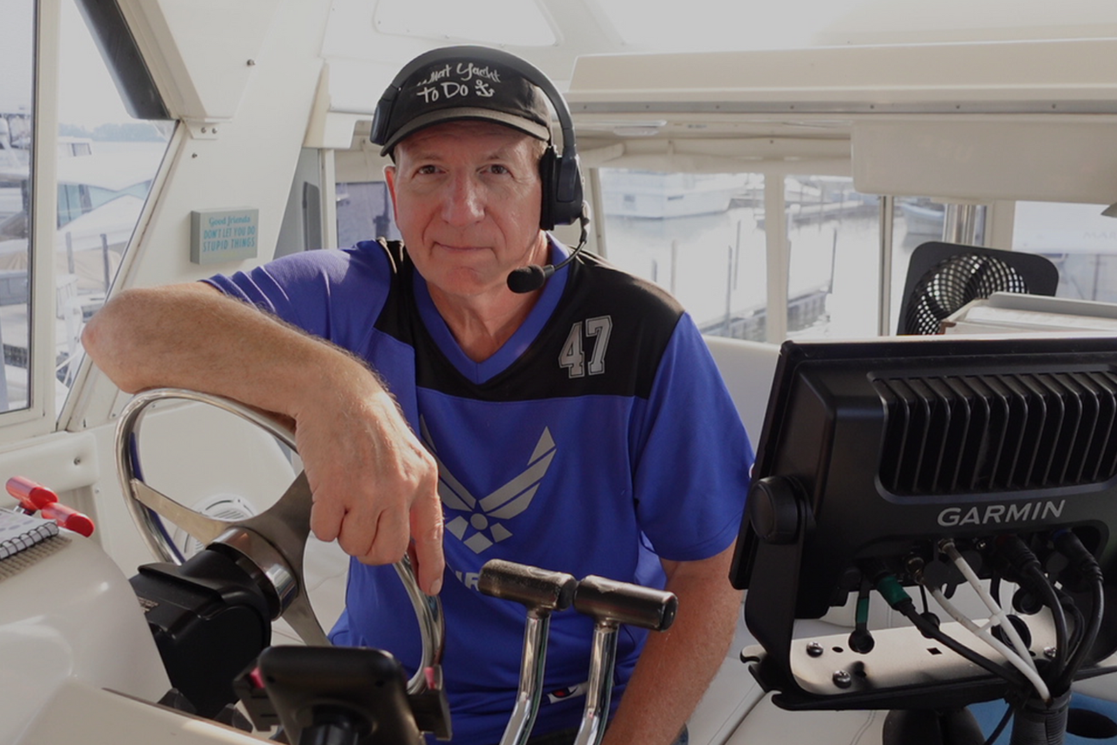 A man wearing a black cap and headset sits at the helm of a boat.
