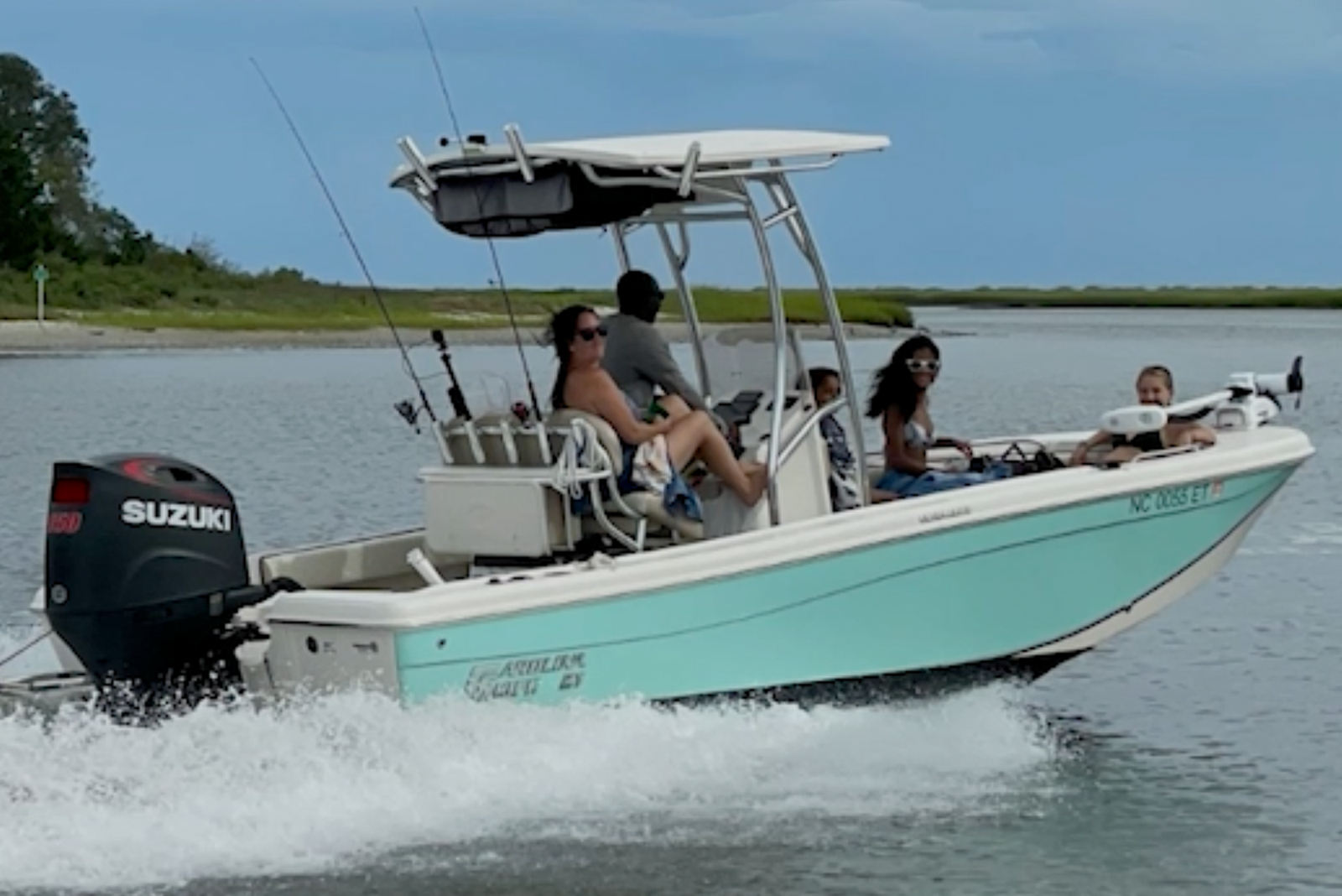 A group of people ride on a small turquoise and white center console fishing boat with a Suzuki outboard motor.