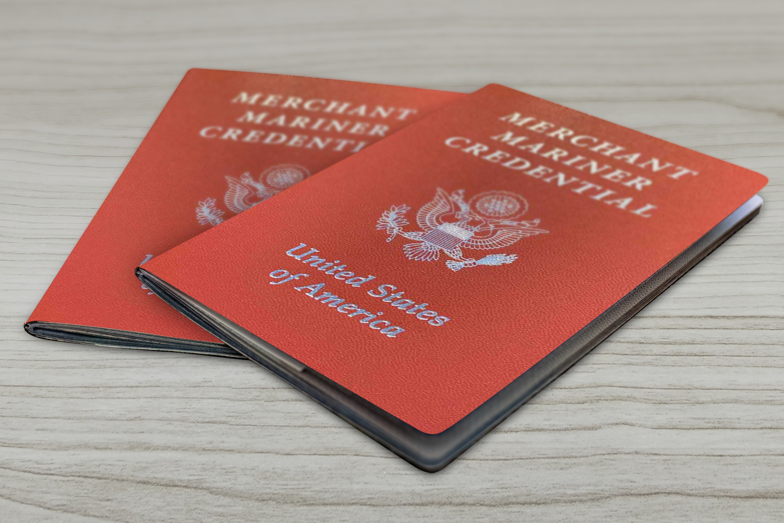 Two U.S. Merchant Mariner Credentials with red covers on a light wooden surface.