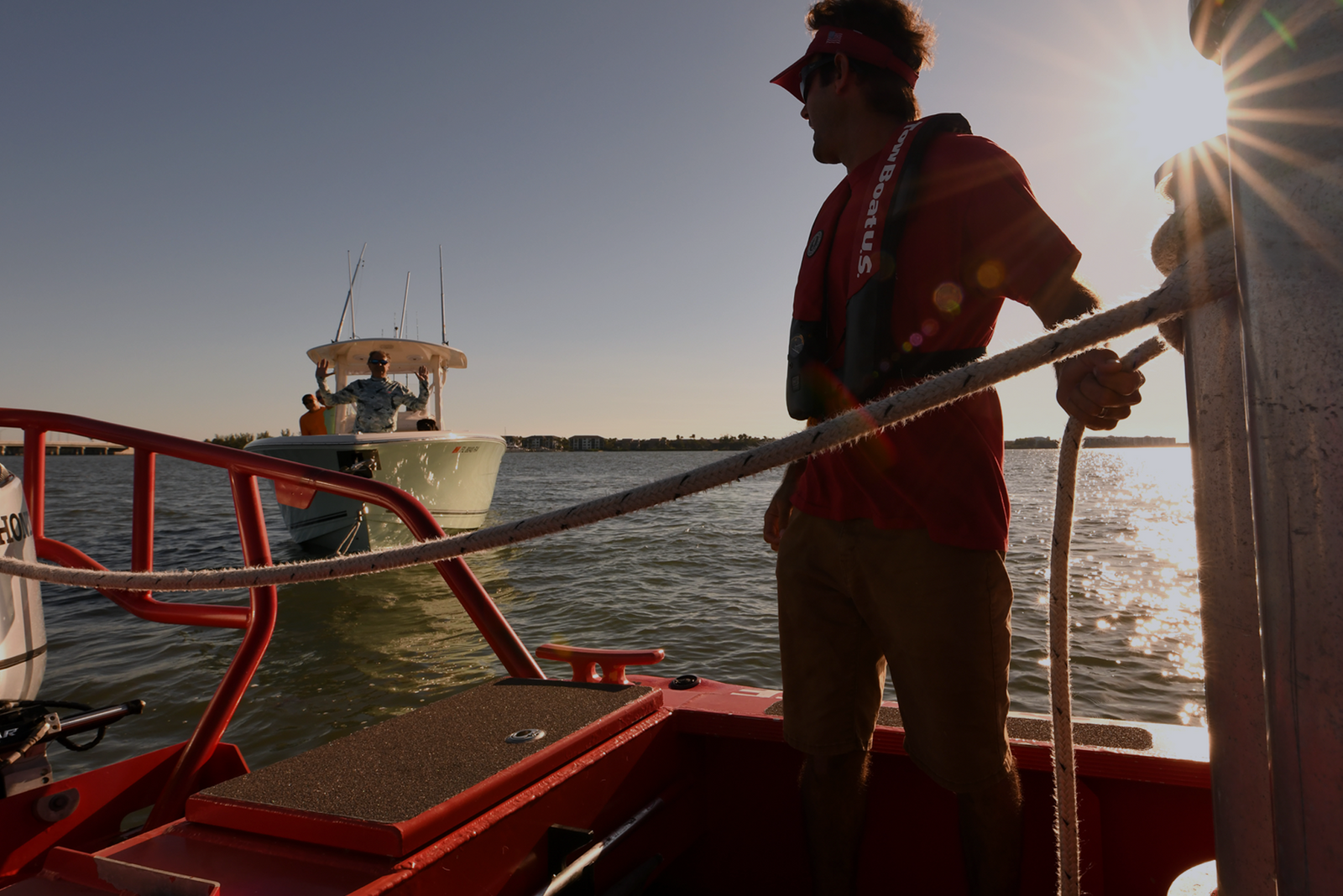 Person on a red boat holding a rope at sunset, with another boat nearby and text about getting a towing endorsement.