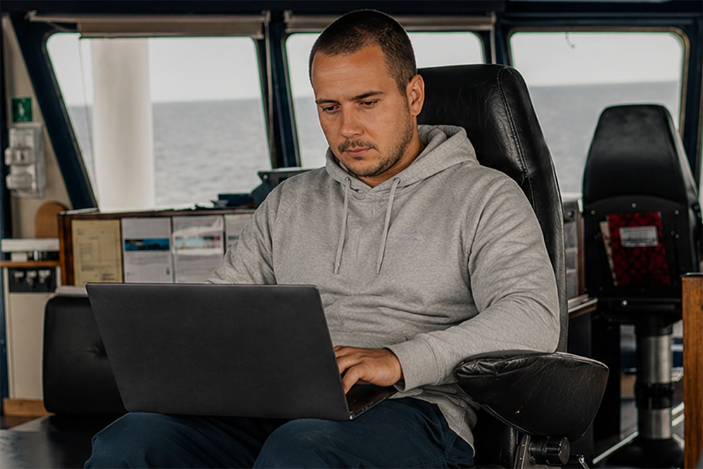 Man seated on a boat with a laptop, working on his charter business plan.