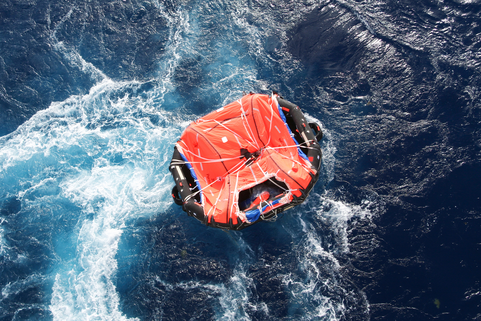 A life raft floating in the open sea amid choppy waters, illustrating the challenge and urgency of how to survive at sea.