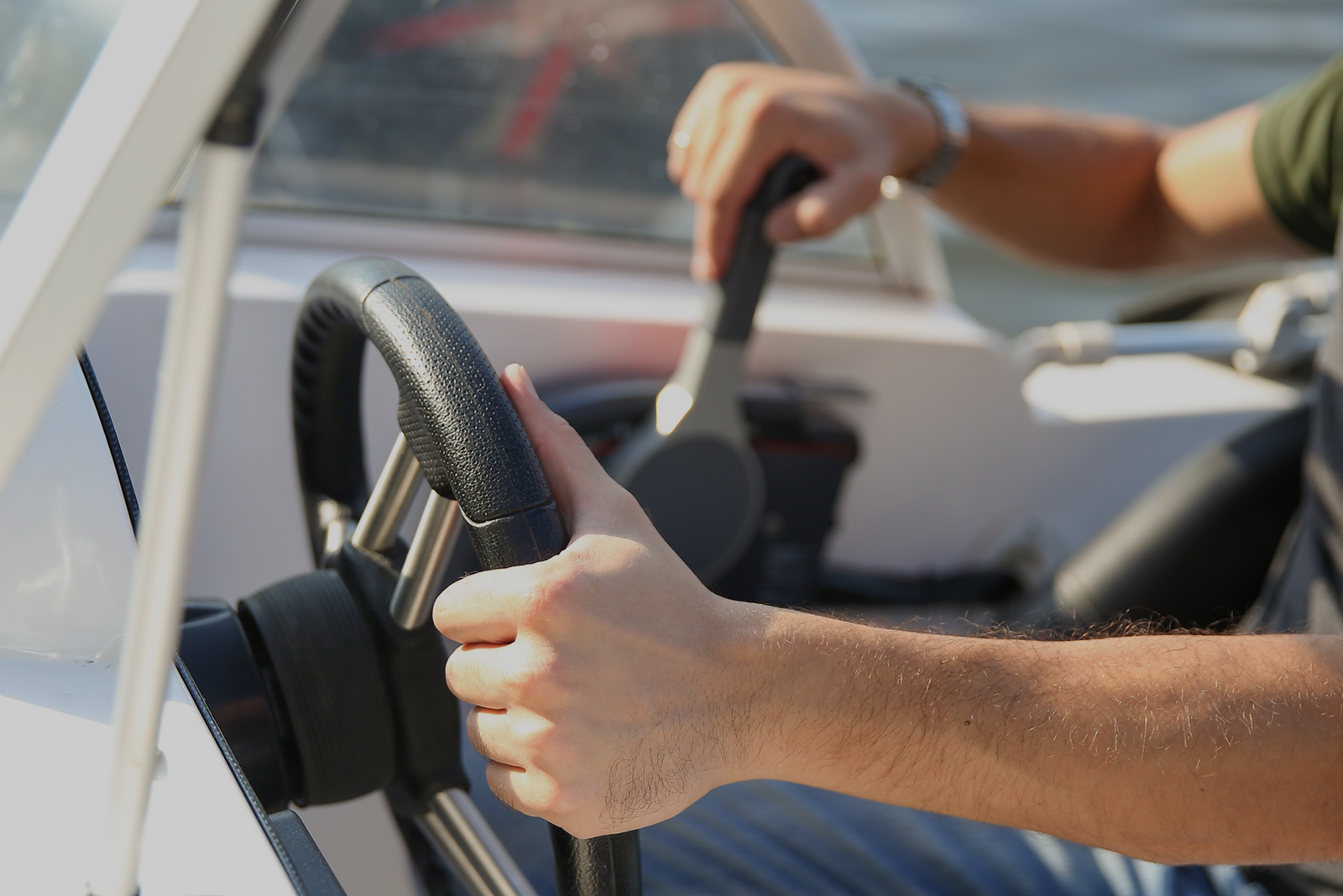 Close-up of a person steering a boat, gripping the wheel and throttle lever.