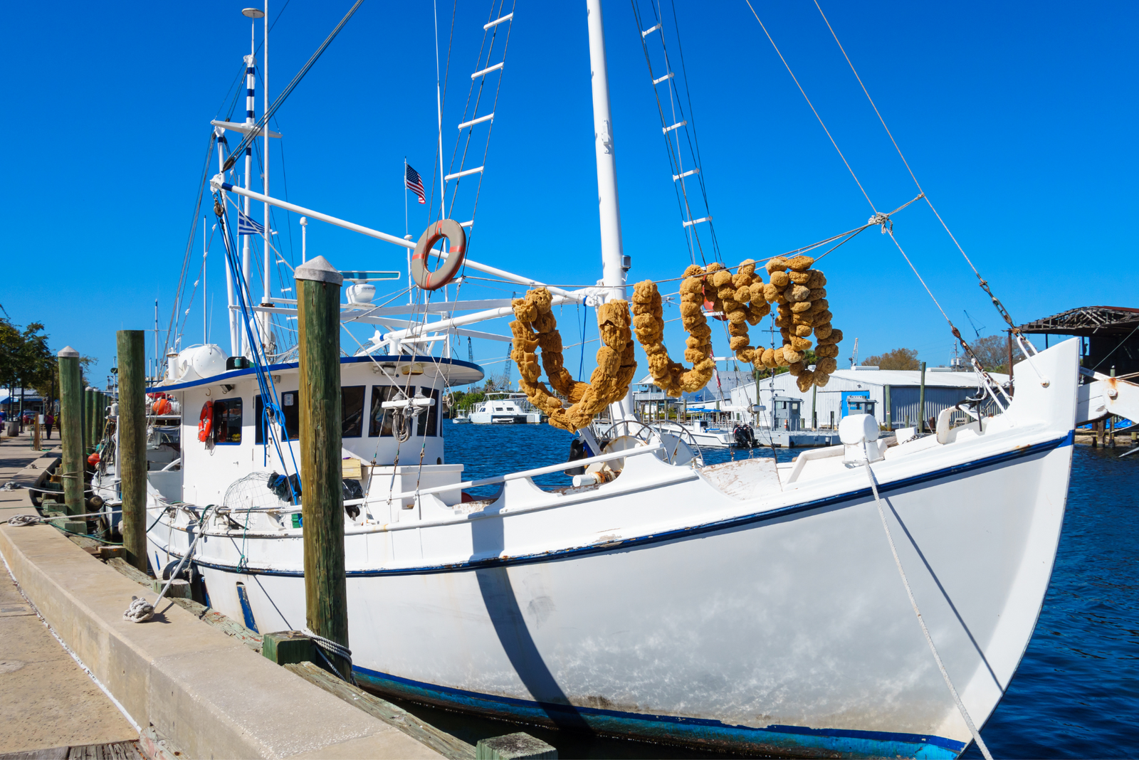 A white boat docked at a marina with sponges hanging from its rigging, symbolizing securing your boat in a private dock.