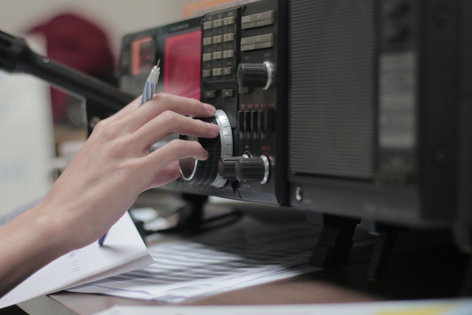 Hand tuning marine radio equipment, documents on desk, and communication device with dials and buttons.