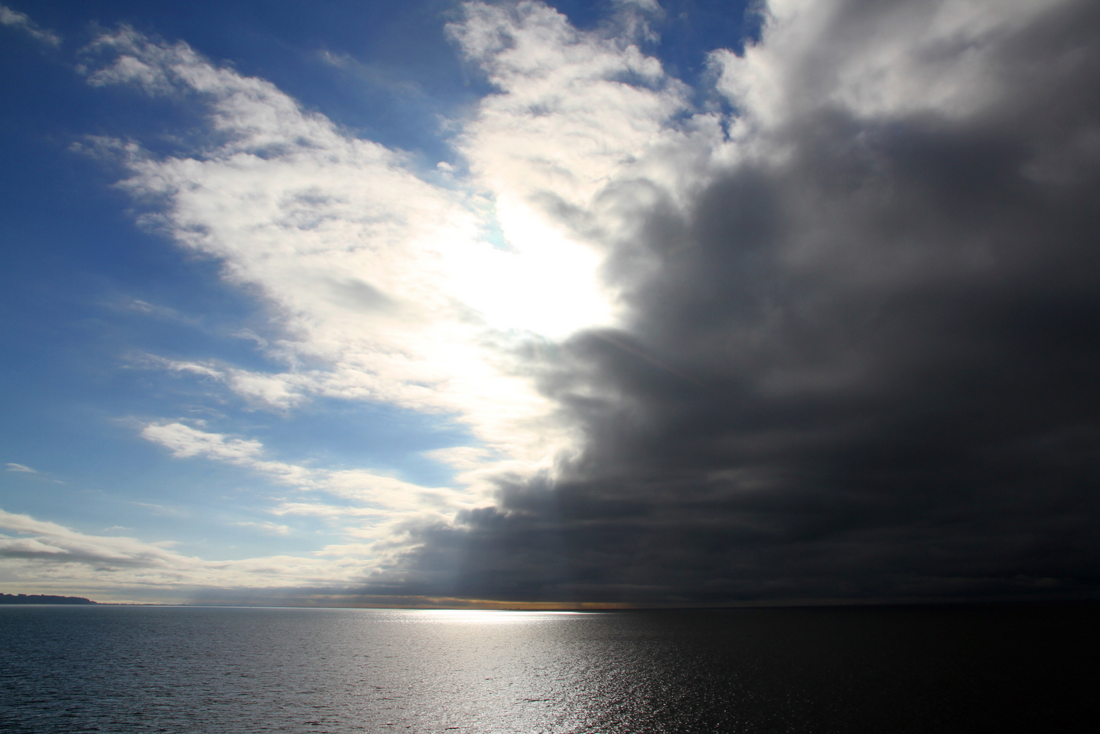 Contrast between bright blue sky and dark storm clouds over a calm ocean, showing an approaching weather front.