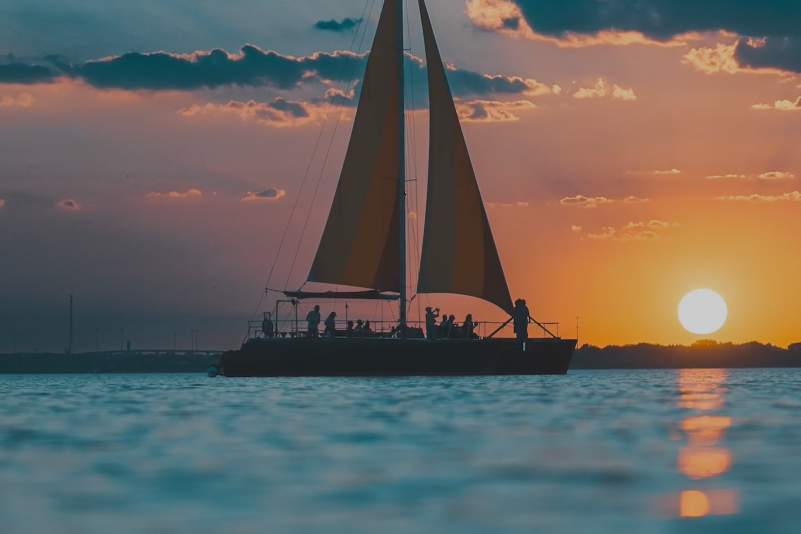 A sailboat silhouetted against a vibrant sunset with people onboard.