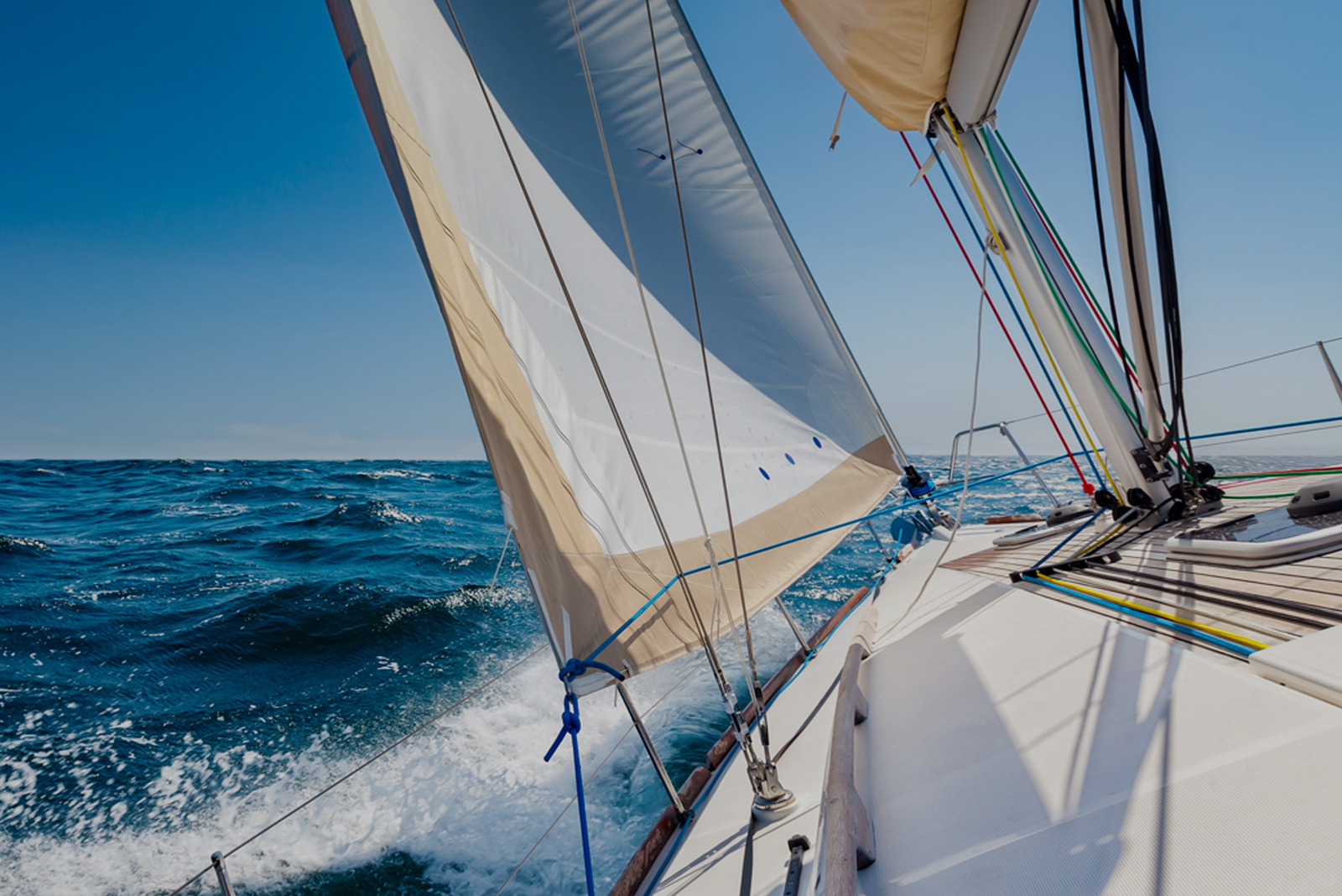 A sailboat cutting through ocean waves under a clear blue sky with sails full of wind.
