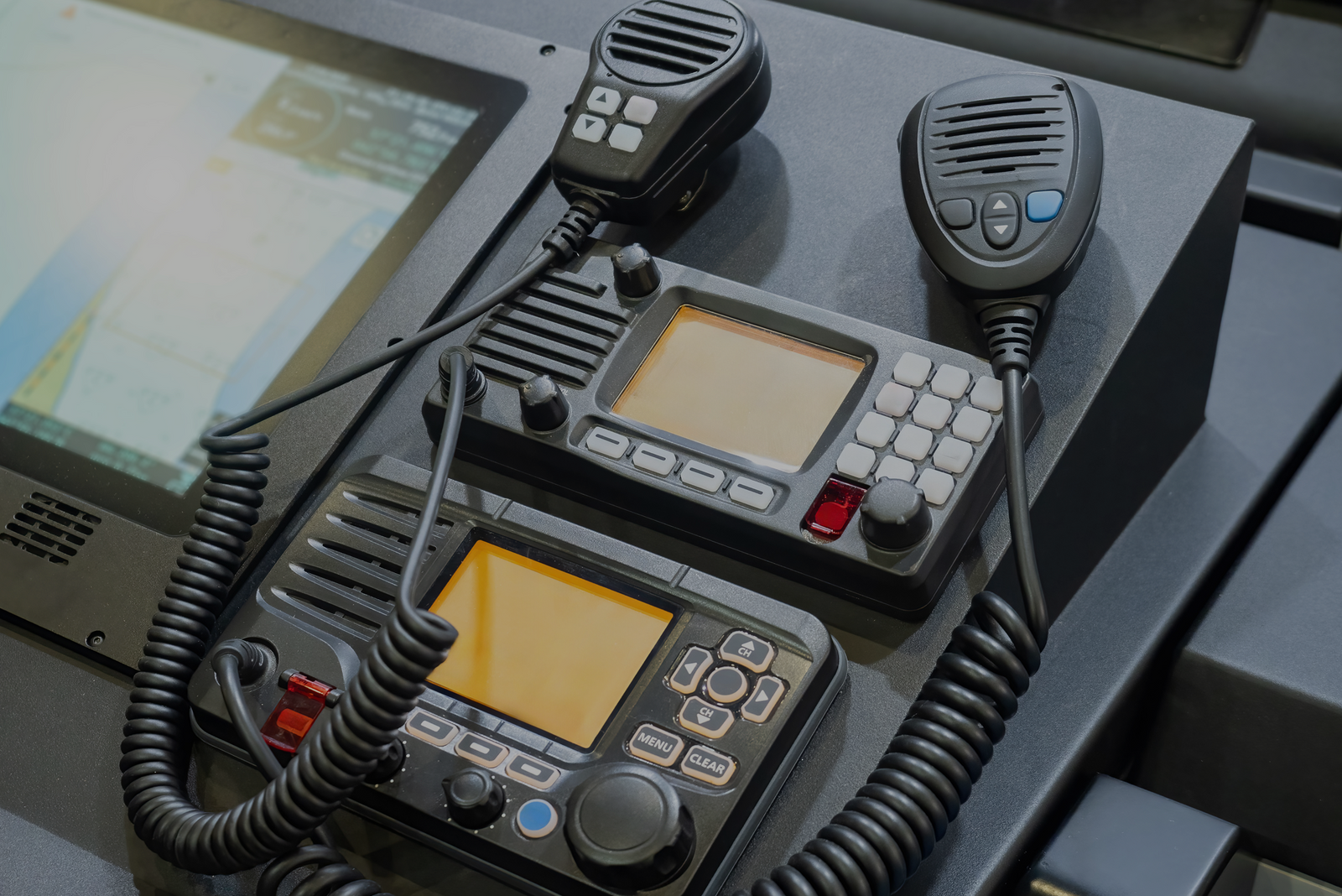 Two mounted VHF marine radios with handheld microphones on a vessel’s console, shown as part of the FCC’s general information for maritime communication licenses.