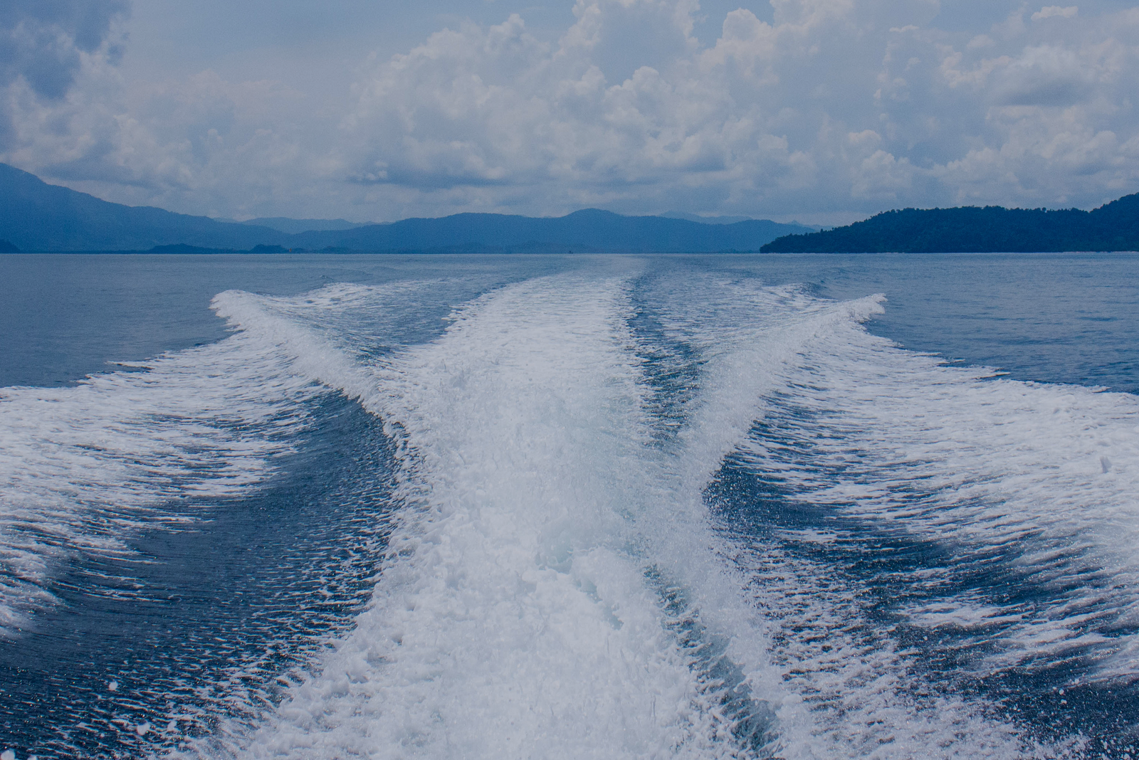 A boat’s wake cuts through open water with distant hills in the background, used to illustrate sea service requirements for a captains license.