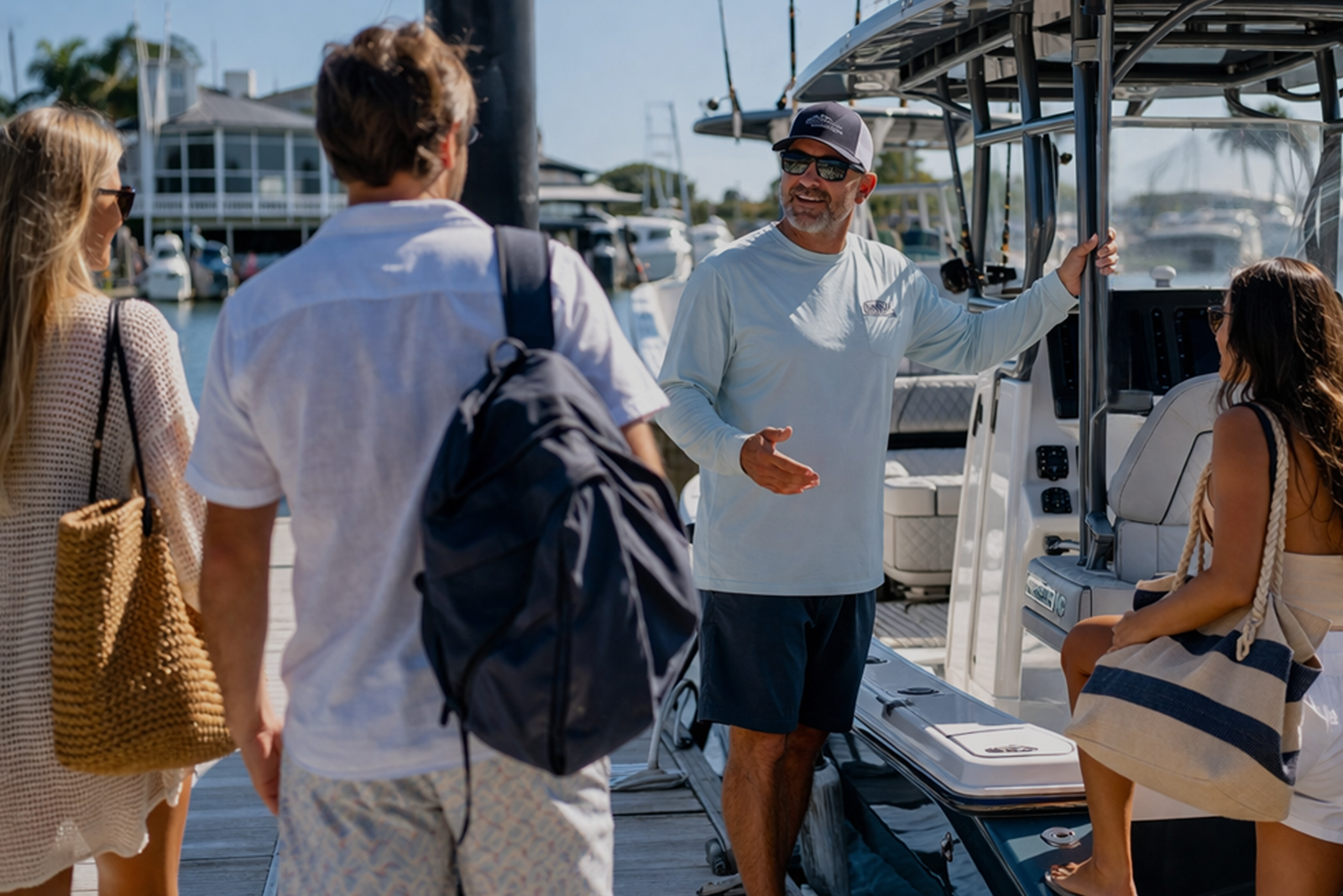 Captain greeting three passengers on a dock beside a charter boat, illustrating the best way to price your boat charter.