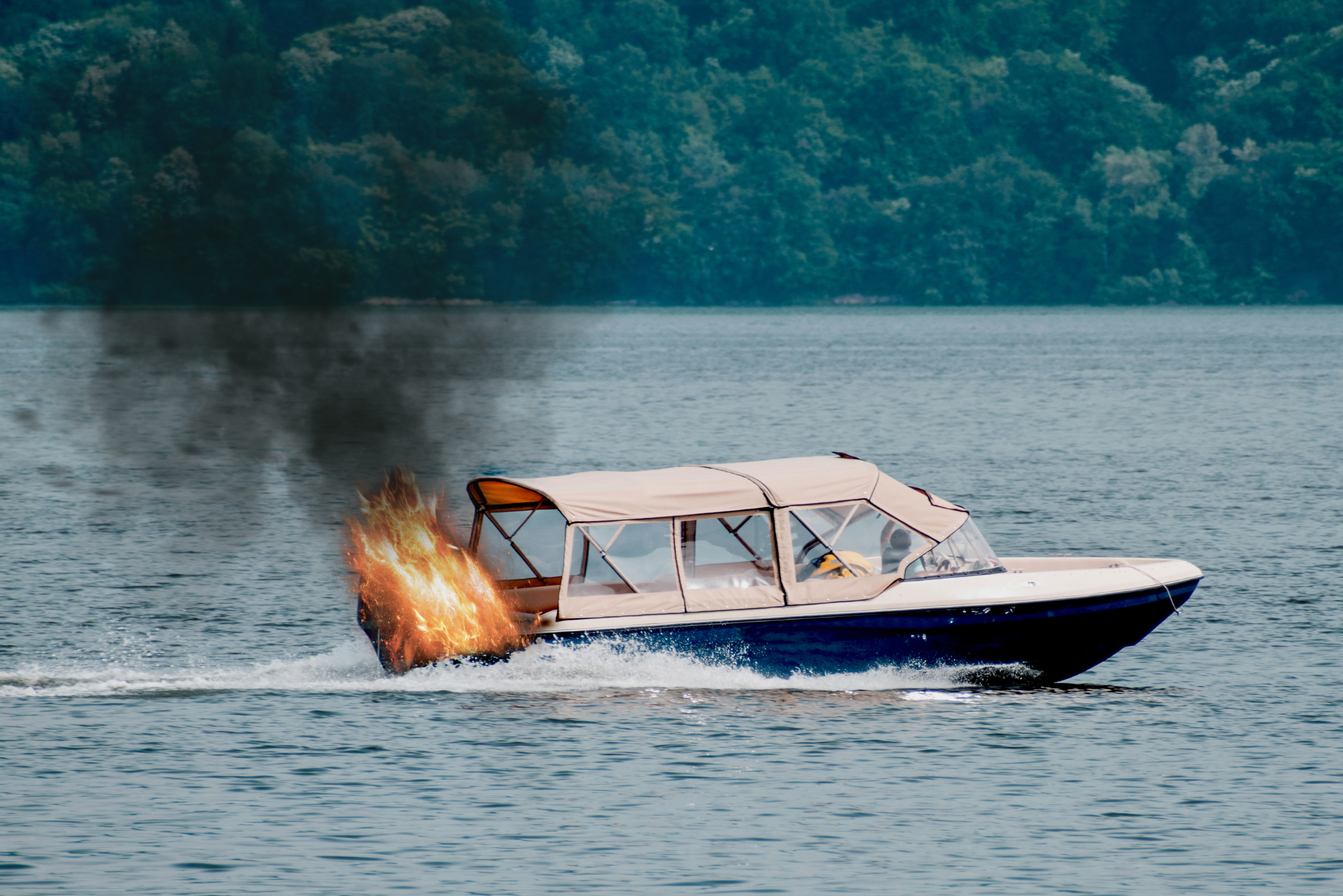 Small boat with a tan canopy engulfed in flames and emitting black smoke.