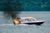 Small boat with a tan canopy engulfed in flames and emitting black smoke.