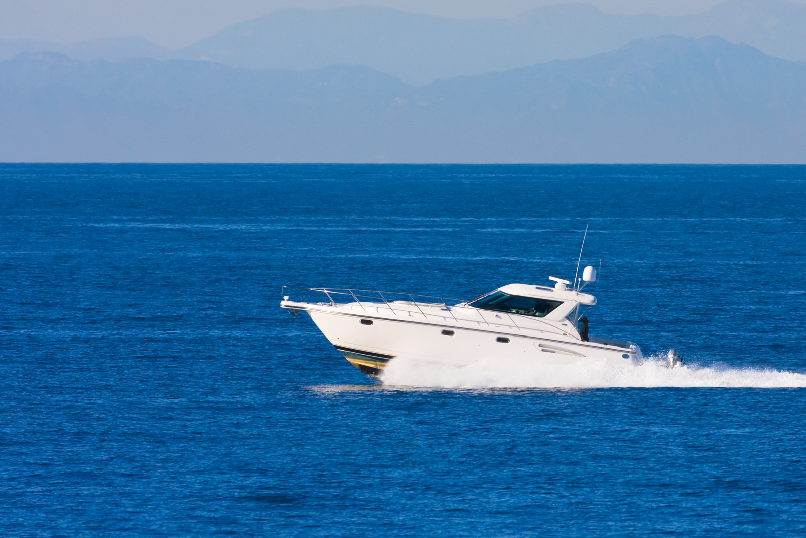 A charter boat crossing in a deep blue ocean waters with mountainous coastline visible in background.