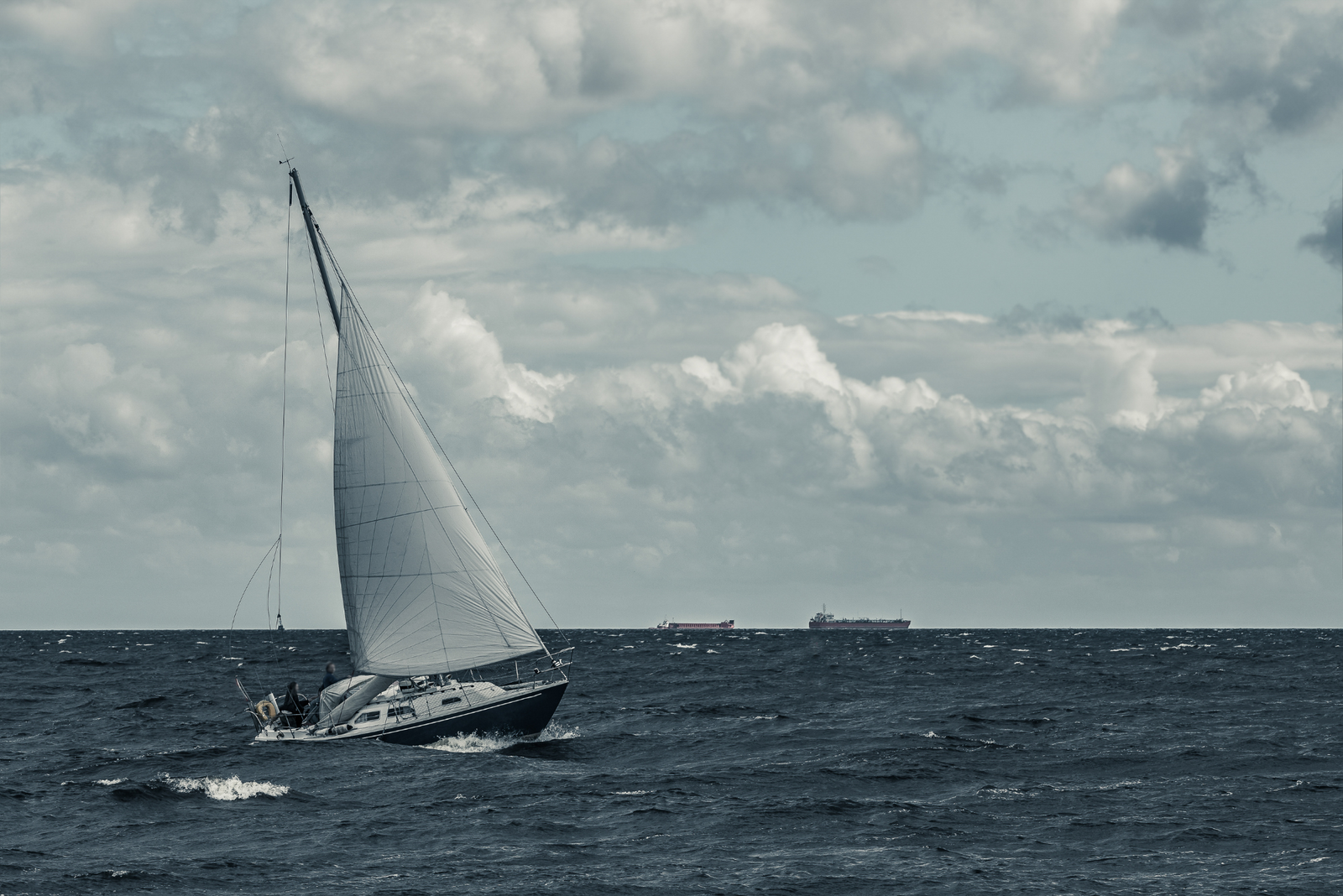 A sailboat navigating choppy waters under a cloudy sky.
